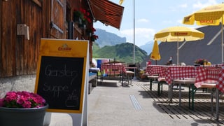 Eine kleine Wirtschaft in den Bergen mit Tischen auf der Terrasse. Daneben stehen gelbe Sonnenschirme.