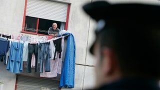 Carabinieri blickt auf Hausfassede, aus der ein Mann blickt. Carabinieri blickt auf Hausfassede, aus der ein Mann blickt.