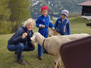 Eine Frau kniet und zwei Kinder stehen neben einem Schaf.