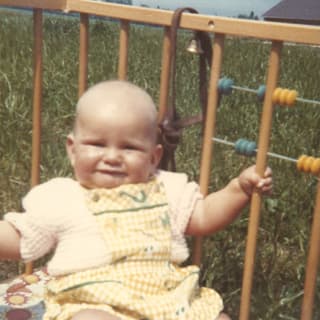 Ein Kleinkind sitzt auf einer Wiese in einem Laufgitter.