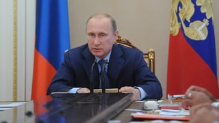 Wladimir Putin sitzt in einem beflaggten Raum