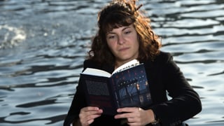 Eine junge Frau liest ein Buch vor einem Brunnen.