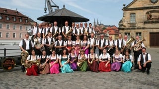 Eine Blasmusikformation mit Musikanten und Musikantinnen in bunten Kleidern.