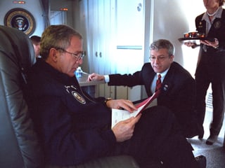 George W. Bush sitzt in einem Sessel an Bord der «Air Force One» und liest ein Papier – neben ihm hockt ein Mitarbeiter.