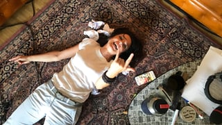 Mona Vetsch auf dem Boden, macht Metal-Handzeichen.