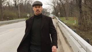Ein Mann mit einem Beret geht auf einer Strasse. Im Hintergrund ist ein Auto zu sehen.