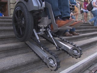 Ein Rollstuhl mit darunter gebauten Raupen fährt rückwärts eine Treppe hinauf.