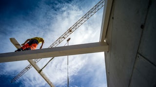 Bauarbeiter auf Stahlgerüst. Bild von unten aufgenommen, der Arbeiter ist also hoch oben und man sieht viel vom blauen Himmel, mit kleinen Wölkchen.