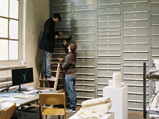 Zwei Männer durchsuchen eine Schublade eines grossen Schubladenregals des St.Galler Werkstoffarchivs.