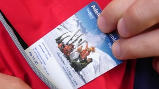 Eine Hand zieht eine Ski-Tageskarte aus einer Jackentasche.
