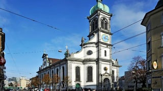 Eine Kirche vom Eingang her fotografiert, oben eine runde Kuppel, die Uhr zeigt 12.15.