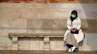 Chinesin mit Gesichtsmaske sitzt einsam auf einer Steinbank. Chinesin mit Gesichtsmaske sitzt einsam auf einer Steinbank.