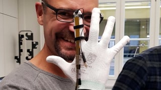 Reto Widmer hält eine Hand hoch mit einem weissen Handschuh, der an einem Finger ein schmales Metallband hat, das als Bremse dient. 