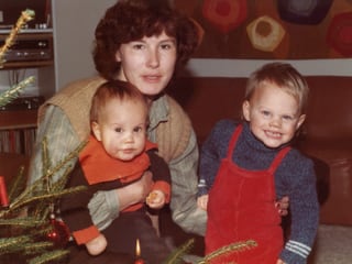 Eine Mutter mit zwei kleinen Kindern neben einem Weihnachtsbaum.