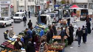 Früchte und Gemüse aufgereiht in Plastikkisten, Menschen stehen darum herum, viele offensichtlich muslimische Ausländer.