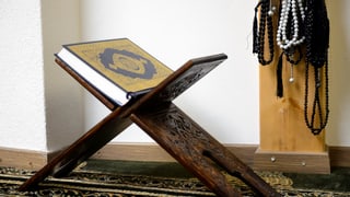 arabischer Schemel mit Koran darauf, daneben aufgehängt Betkränze