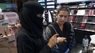 Verhüllte Mitarbeiterin berät eine Kundin in der Kosmetikabteilung. Verhüllte Mitarbeiterin berät eine Kundin in der Kosmetikabteilung.