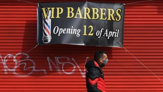 Eine Person mit Maske geht an einem Plakat vorbei, das ankündigt, dass ab Montag ein Friseur wieder öffnet.