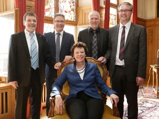 Frau sitzt in Stuhl, dahinter vier Herren stehend