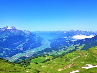 Blick von einer grünen Alpmatte ins Tal, es herrscht wolkenloses wetter