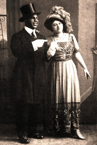 Mann in Anzug und Zylinder, Frau mit schickem Kleid und Hut mit Feder.