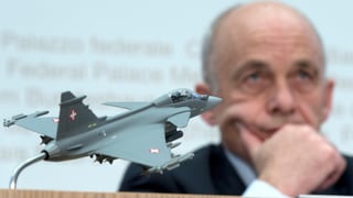 Ein nachdenklicher Ueli Maurer sitzt hinter einem Modell des Gripen.