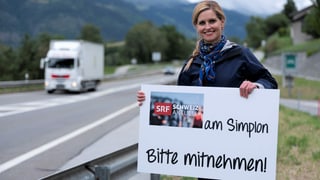 Sabine Dahinden mit dem Schild "Schweiz Aktuell am Simplon" an einer Strasse