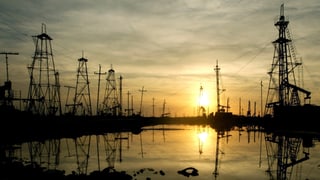 Öl-Bohrtürme vor der aufgehenden Sonne, davor ein Ölfeld. Aufgenommen in Baku (Aserbaidschan). 
