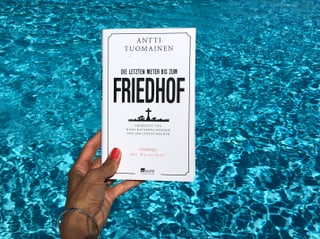 Annette König hält das Buch von Antti Tuomainen: «Die letzten Meter bis zum Friedhof» vor blaues Wasser Annette König hält das Buch von Antti Tuomainen: «Die letzten Meter bis zum Friedhof» vor blaues Wasser