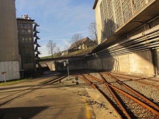 Blick über alte Bahngeleise zu einigen baufälligen Fabrikgebäuden.