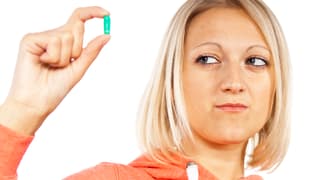 Eine Frau beäugt eine Tablette zwischen ihren Fingern skeptisch.