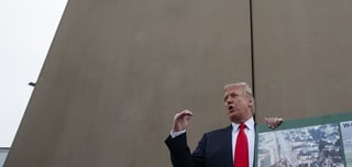 Donald Trump vor einer hohen grauen Betonmauer.
