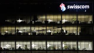 Mehrstöckiges, transparentes Gebäude mit Swisscom-Logo: Es ist dunkel und in den Büros wird gearbeitet. Mehrstöckiges, transparentes Gebäude mit Swisscom-Logo: Es ist dunkel und in den Büros wird gearbeitet.