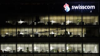 Mehrstöckiges, transparentes Gebäude mit Swisscom-Logo: Es ist dunkel und in den Büros wird gearbeitet.