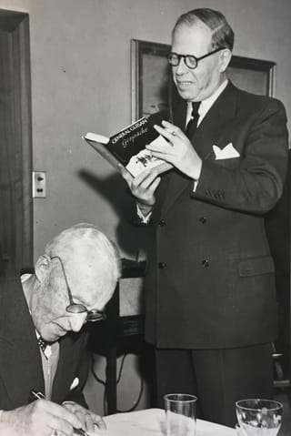 Zwei Männer, einer steht und liest ein Buch. Der andere schreibt etwas. Zwei Männer, einer steht und liest ein Buch. Der andere schreibt etwas.