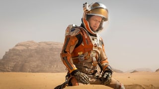 Matt Damon in einer Sandlandschaft. Er ist ein Astronaut.