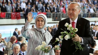 Erdogan und Frau mit Kopftuch vor Menge. Er hat Blumen in der Hand.