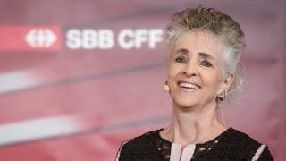Regierungsrätin Carmen Walker Späh lachend und mit grau-meliertem Haar vor einem SBB-Logo.