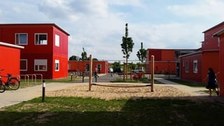 Ein Klettergerüst steht inmitten roter Container-Häuser.