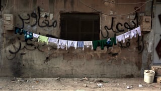 Symbolbild: Wäscheleine mit trocknender Kleidung vor beschädigtem Haus.