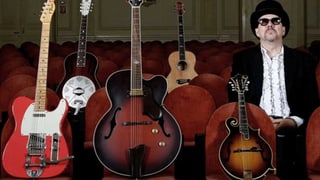 Zu sehen ist Pink Pedrazzi. Er sitz mit Sonnen brille und Zylinder. Neben ihm sind auf fünf Stühlen fünf Gitarren placiert.