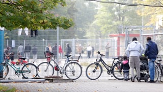 Menschen stehen vor und hinter einem Gitterzaun, der das Gelände umschliesst.