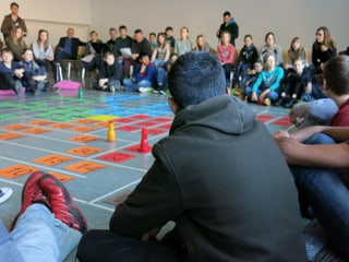 Kinder sitzen am Boden vor einem grossen Spiel mit Würfel und Figuren.