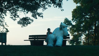 Kind mit riesigem überlebensgrossen Teddy auf Gartenbank sitzend.