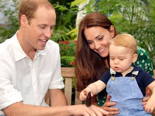 Prinz George auf der Schoss von Kate sitzend zeigt auf einen Schmetterling der auf Williams Hand platzgenommen hat.