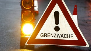 Dreieck mit der Aufschrift Grenzwacht. Daneben leuchtet eine orangene Ampel. Dreieck mit der Aufschrift Grenzwacht. Daneben leuchtet eine orangene Ampel.