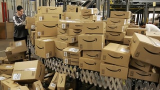 Ein Mann beim Sortieren eines Bergs Kartonschachteln, die als solche des Onlinehändlers Amazon zu erkennen sind.