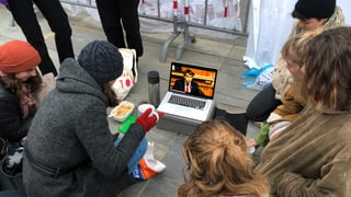 Junge Menschen sitzen am Boden rund um einen Laptop.