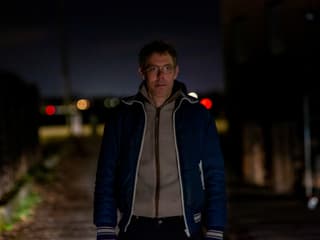 Mann mit kurzen Haaren, Brille und blauer Trainigsjacke in einem nächtlichen Industriegebiet. Mann mit kurzen Haaren, Brille und blauer Trainigsjacke in einem nächtlichen Industriegebiet.