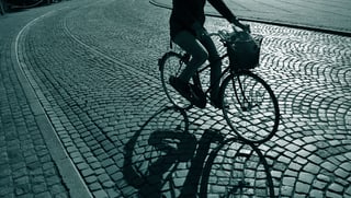 Velofahrer auf einer Kopfsteinpflasterstrasse im Morgengrauen.